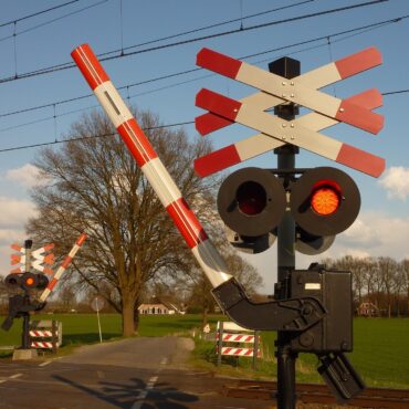 Railroad crossing with lowered barriers, red flashing lights, and tracks in the foreground in a rural setting