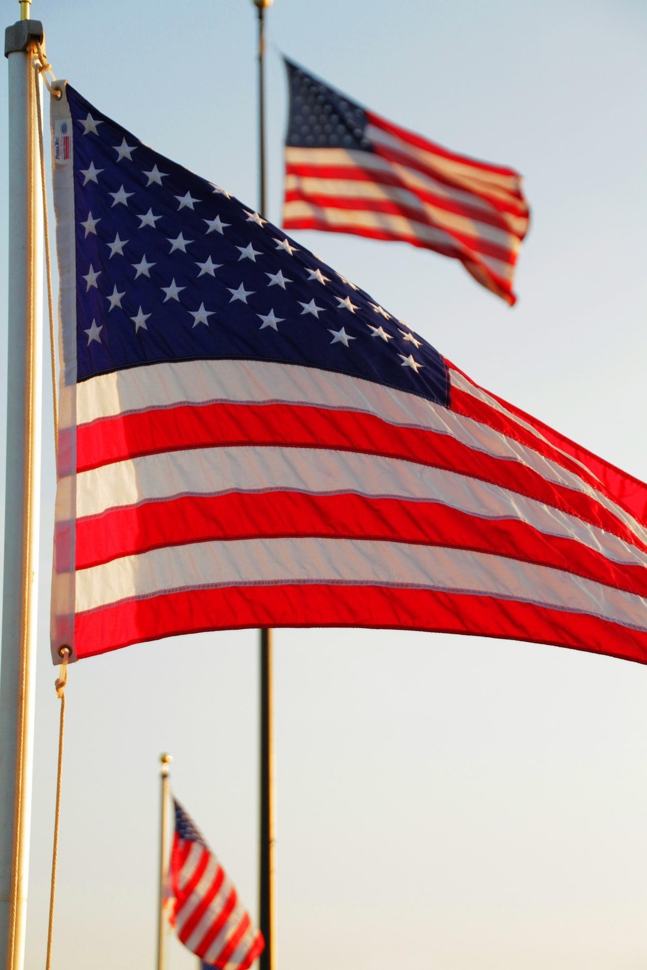 American flag waving on a flagpole against a clear blue sky, with another flag visible in the background
