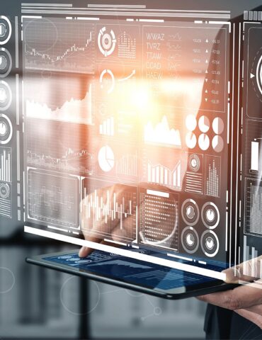 Business professional holding a tablet with holographic data dashboards and charts projected in front of him/her.