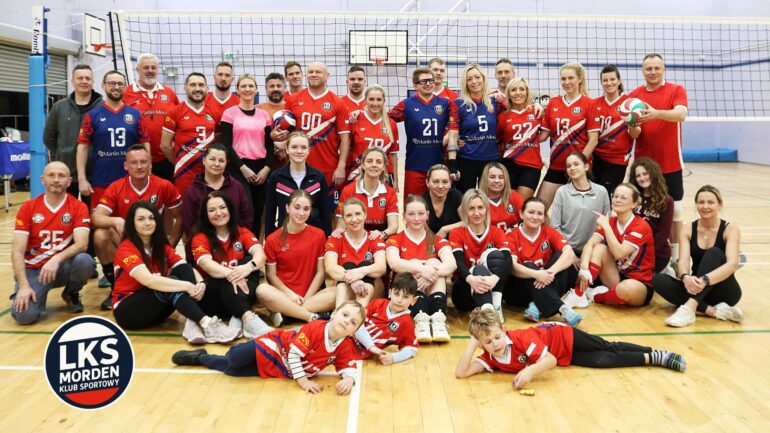 Kibice LKS Morden - NOTE.radio - Polskie radio w UK | Polskie radio w Londynie Large group of volleyball players in red uniforms posing together in a gym with a net behind them and a team logo in the foreground.