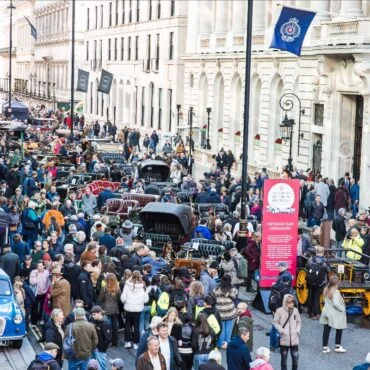 Crowded city street during a vintage car show with classic cars lined along the curb and onlookers.