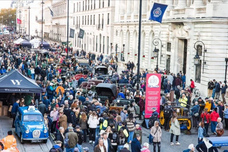 Crowded city street during a vintage car show with classic cars lined along the curb and onlookers.