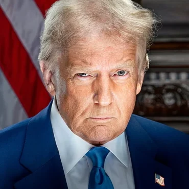 Serious portrait of a man in a blue suit and blue tie, with an American flag in the background.