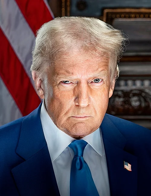 Serious portrait of a man in a blue suit and blue tie, with an American flag in the background.