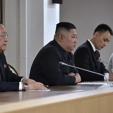 Four panelists seated at a long conference table with microphones, participating in a formal meeting.