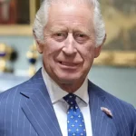 Older man in a blue pinstripe suit with a pink boutonniere at a formal event.