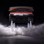 Rear view of a sports car lifting off the ground, exhaust flames and billowing smoke beneath against a dark backdrop