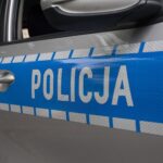 Polish police car door with blue livery and white POLICJA text; silver door handle and checkered pattern along the side