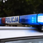 Polish police car roof with blue and red emergency lights blinking, POLICJA visible on the side bar.