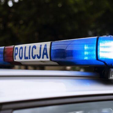 Polish police car roof with blue and red emergency lights blinking, POLICJA visible on the side bar.
