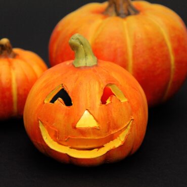 Three carved pumpkins sit on a dark surface, with the front pumpkin smiling and the others in the background.
