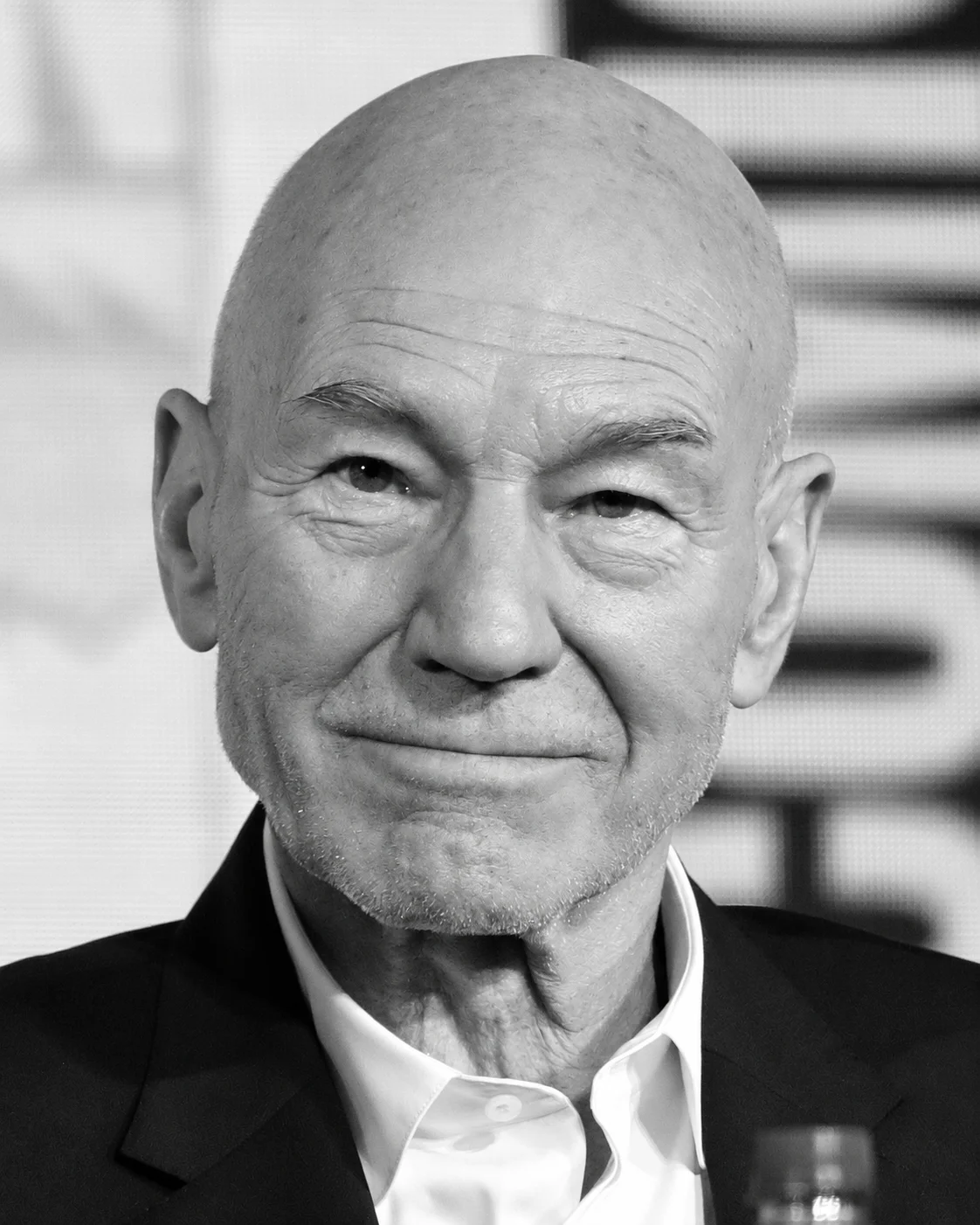 Close-up black-and-white portrait of a smiling, bald man in a suit and white shirt.