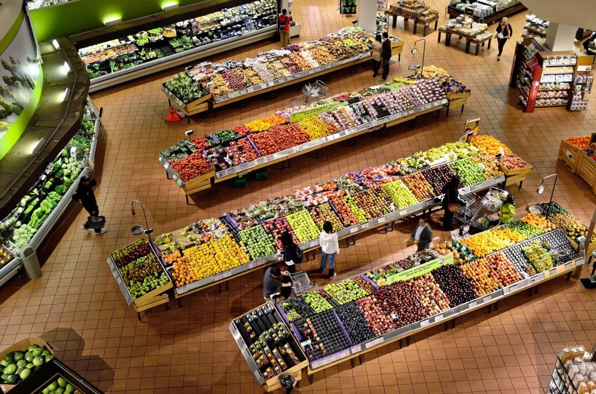Bird's-eye view of a supermarket produce department with long rows of fruits and vegetables beyond tiled floors.