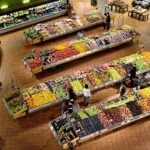 Bird's-eye view of a supermarket produce department with long rows of fruits and vegetables beyond tiled floors.