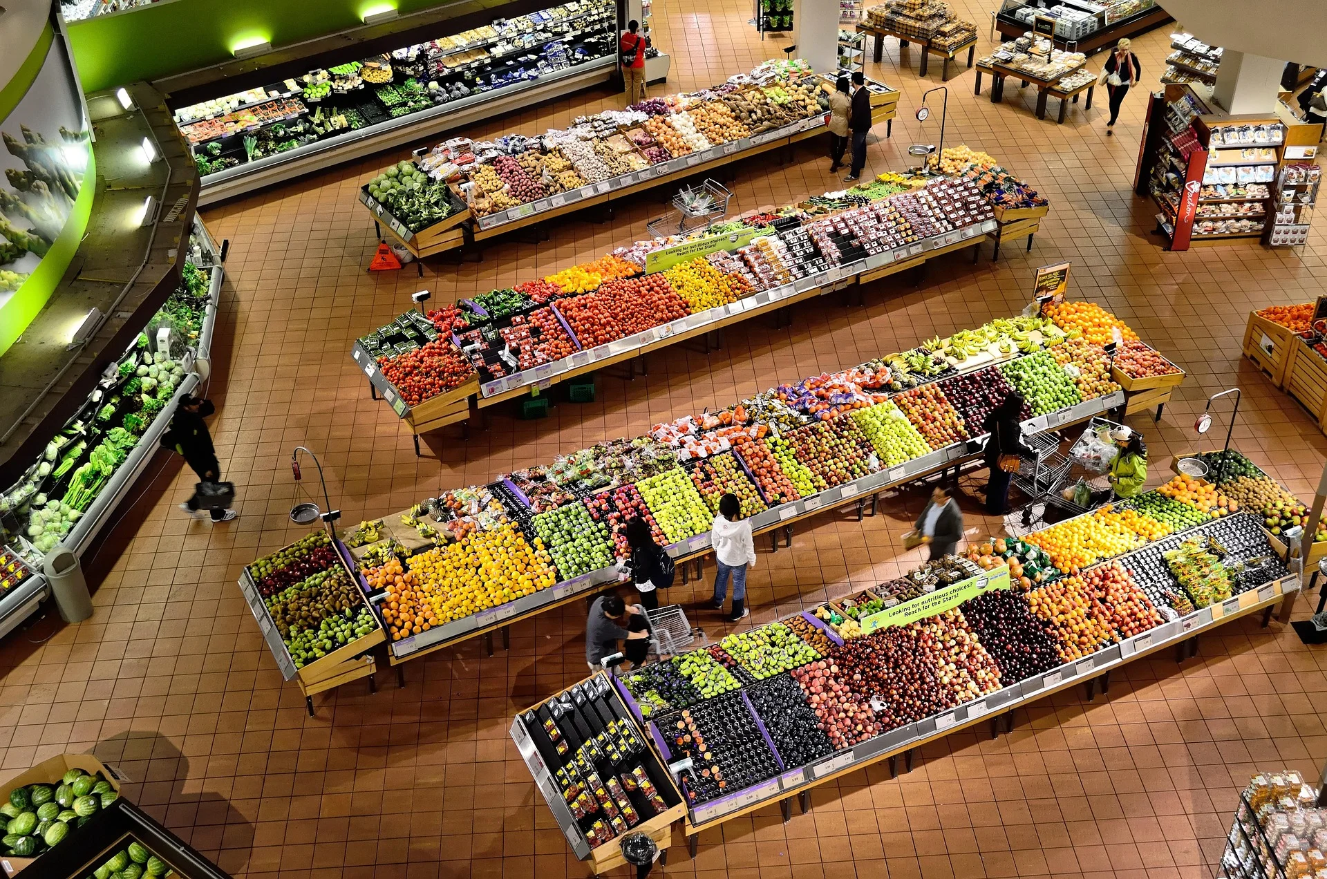 Bird's-eye view of a supermarket produce department with long rows of fruits and vegetables beyond tiled floors.