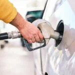 Close-up of a hand inserting a fuel nozzle into a car's gas tank during refueling