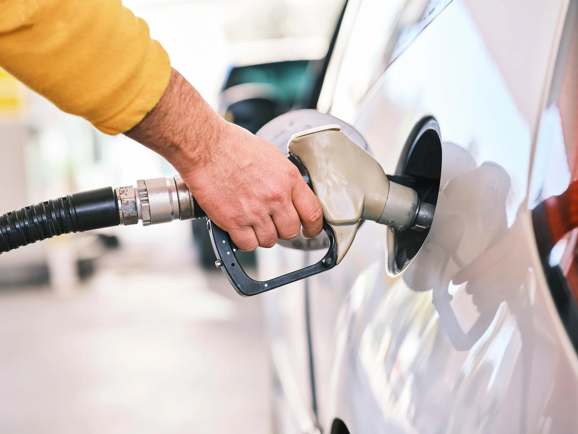Close-up of a hand inserting a fuel nozzle into a car's gas tank during refueling