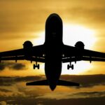 Silhouette of a jet airliner descending for landing against a golden sunset sky with extended landing gear down.