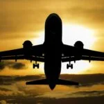 Silhouette of a jet airliner descending for landing against a golden sunset sky with extended landing gear down.