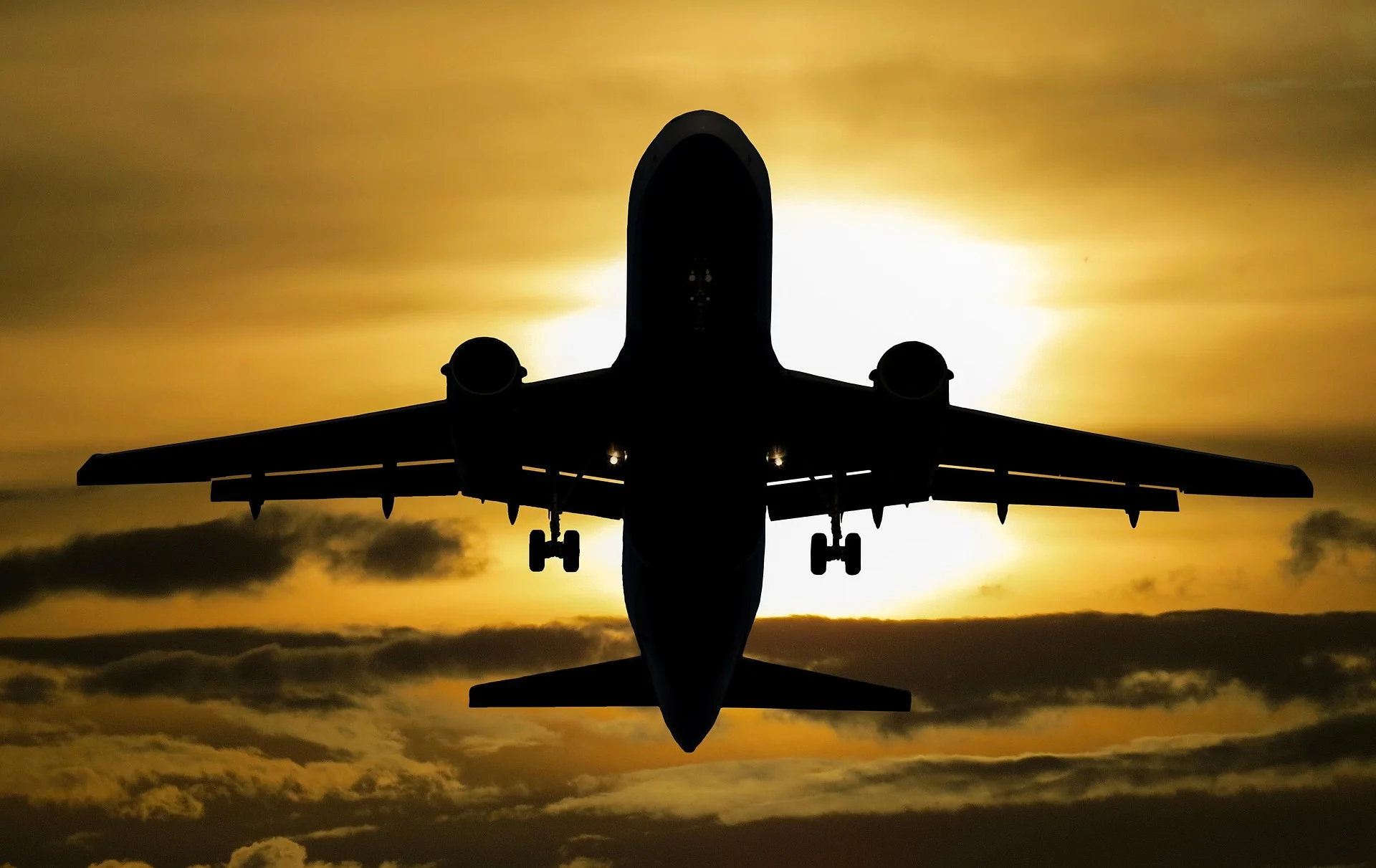 Silhouette of a jet airliner descending for landing against a golden sunset sky with extended landing gear down.