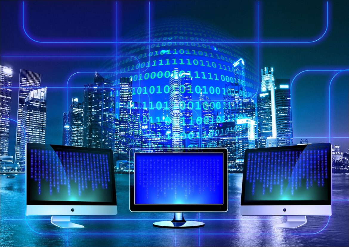 Futuristic city skyline at night with blue neon lines overlaid and three monitors showing binary code.
