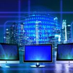 Futuristic city skyline at night with blue neon lines overlaid and three monitors showing binary code.