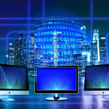 Futuristic city skyline at night with blue neon lines overlaid and three monitors showing binary code.