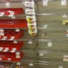 Empty grocery store bakery aisle with red baking pans stacked on shelves and a vertical rack of white circular burger presses in the center.
