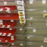 Empty grocery store bakery aisle with red baking pans stacked on shelves and a vertical rack of white circular burger presses in the center.