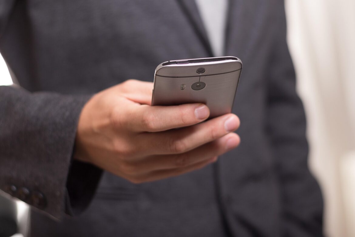 Person in a dark suit holding a silver smartphone with a rear camera