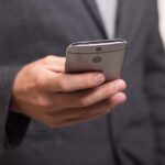 Person in a dark suit holding a silver smartphone with a rear camera