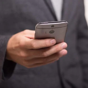 Person in a dark suit holding a silver smartphone with a rear camera