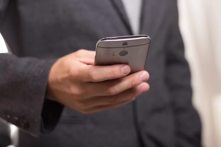 Person in a dark suit holding a silver smartphone with a rear camera