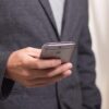 Hands holding a silver smartphone in a dark blazer; close-up of device and hands.