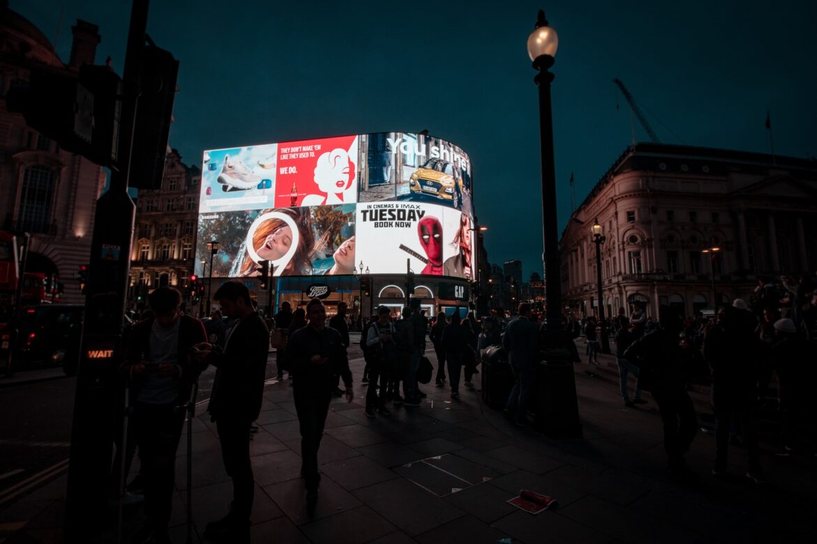 Night scene at Piccadilly Circus with a large curved digital billboard displaying ads and pedestrians below.