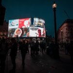 Night scene at Piccadilly Circus with a large curved digital billboard displaying ads and pedestrians below.