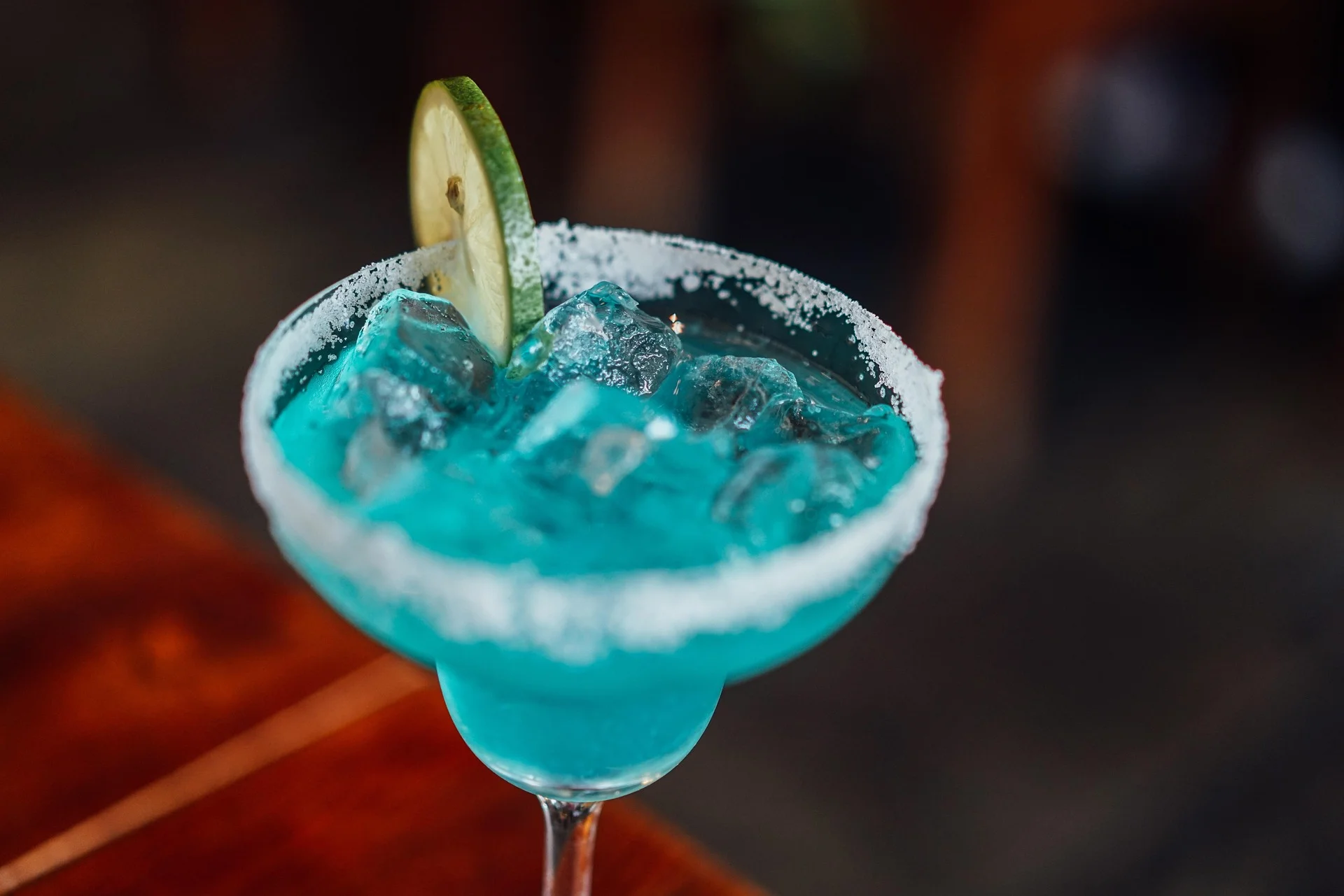 Turquoise margarita in a salted rim glass with a lime wheel garnish and ice-filled drink close up.