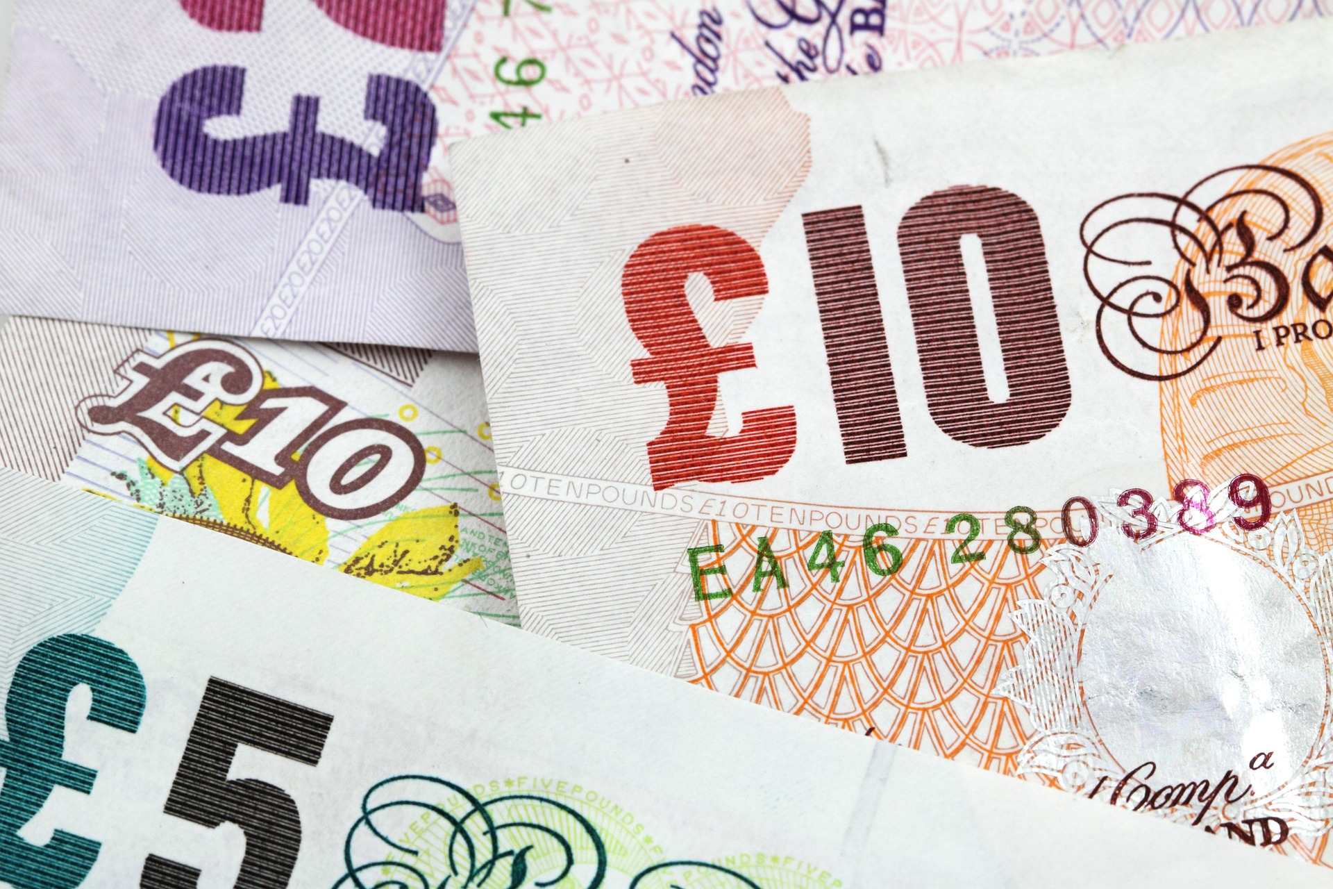 Close-up of overlapping euro banknotes, showing a red 100€ note and other denominations with intricate patterns.
