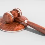 Judge's wooden gavel resting on a polished round sound block, with a subtle shadow on a light background.