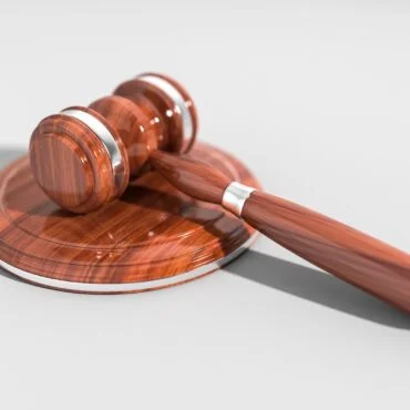 Judge's wooden gavel resting on a polished round sound block, with a subtle shadow on a light background.