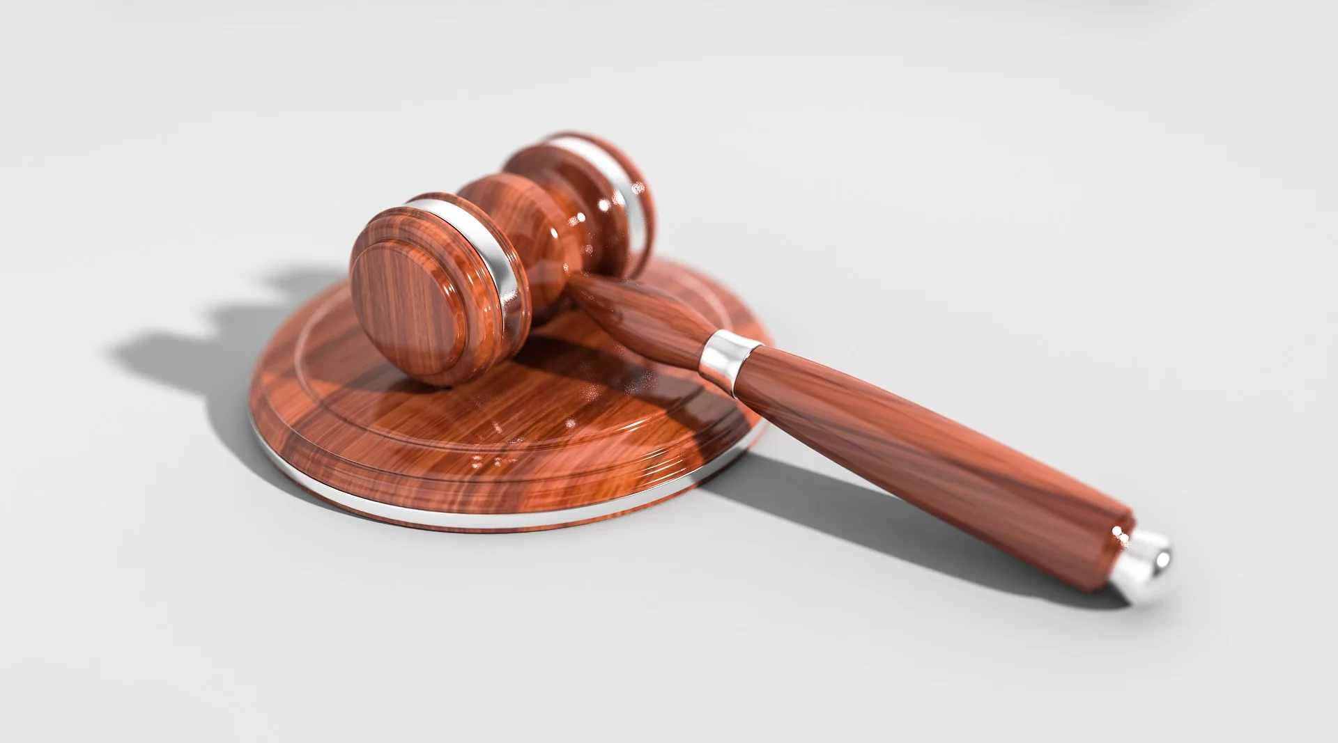 Judge's wooden gavel resting on a polished round sound block, with a subtle shadow on a light background.