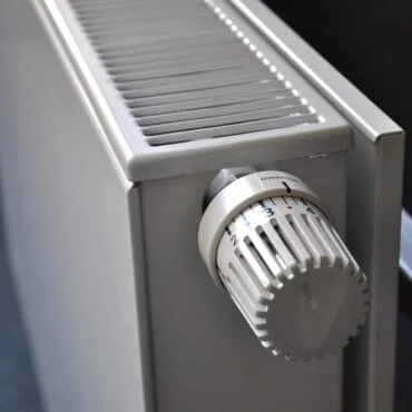 Close-up of a white radiator thermostat knob on a gray radiator, with a numbered dial (1–4).
