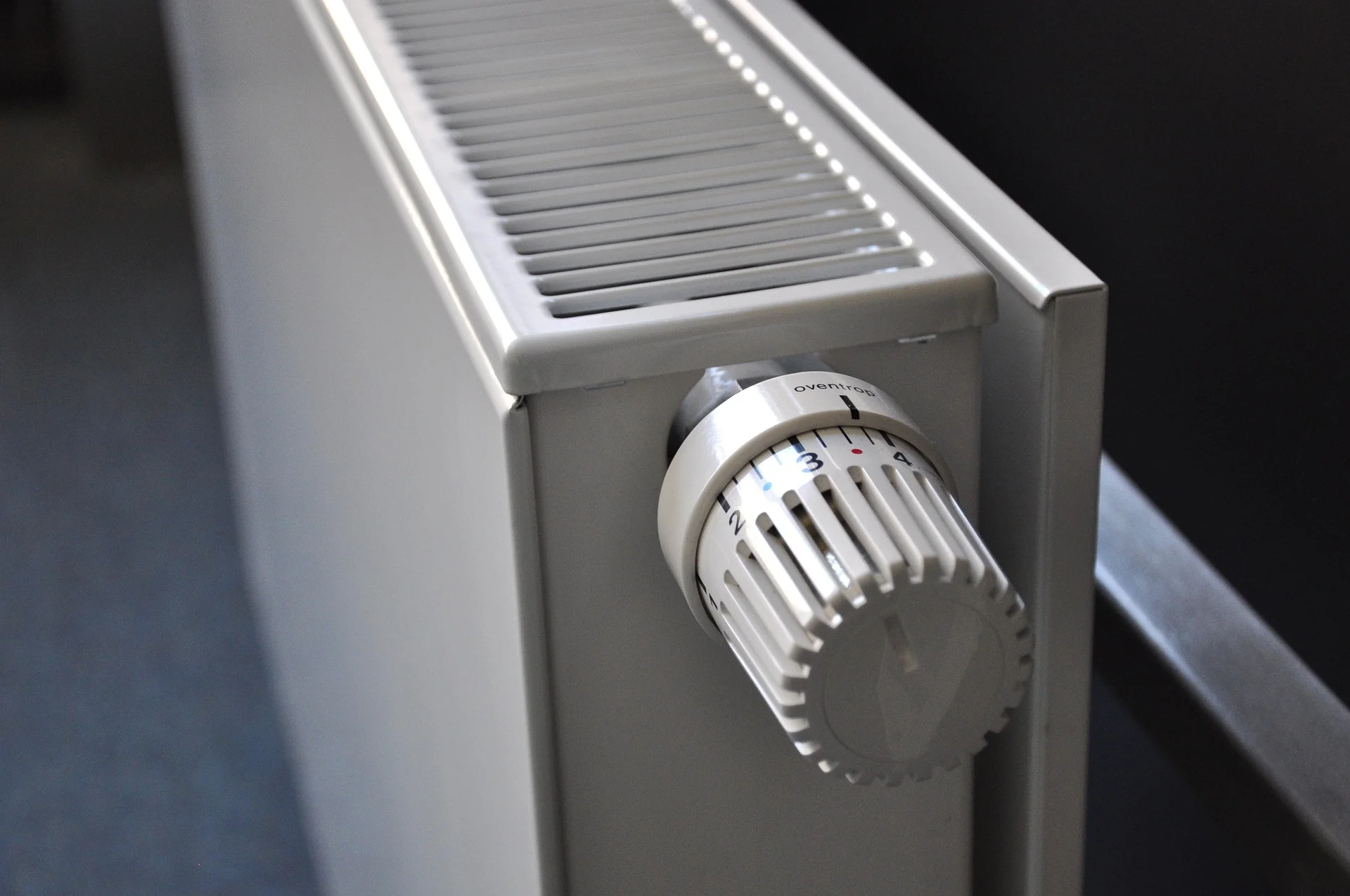 Close-up of a white radiator thermostat knob on a gray radiator, with a numbered dial (1–4).
