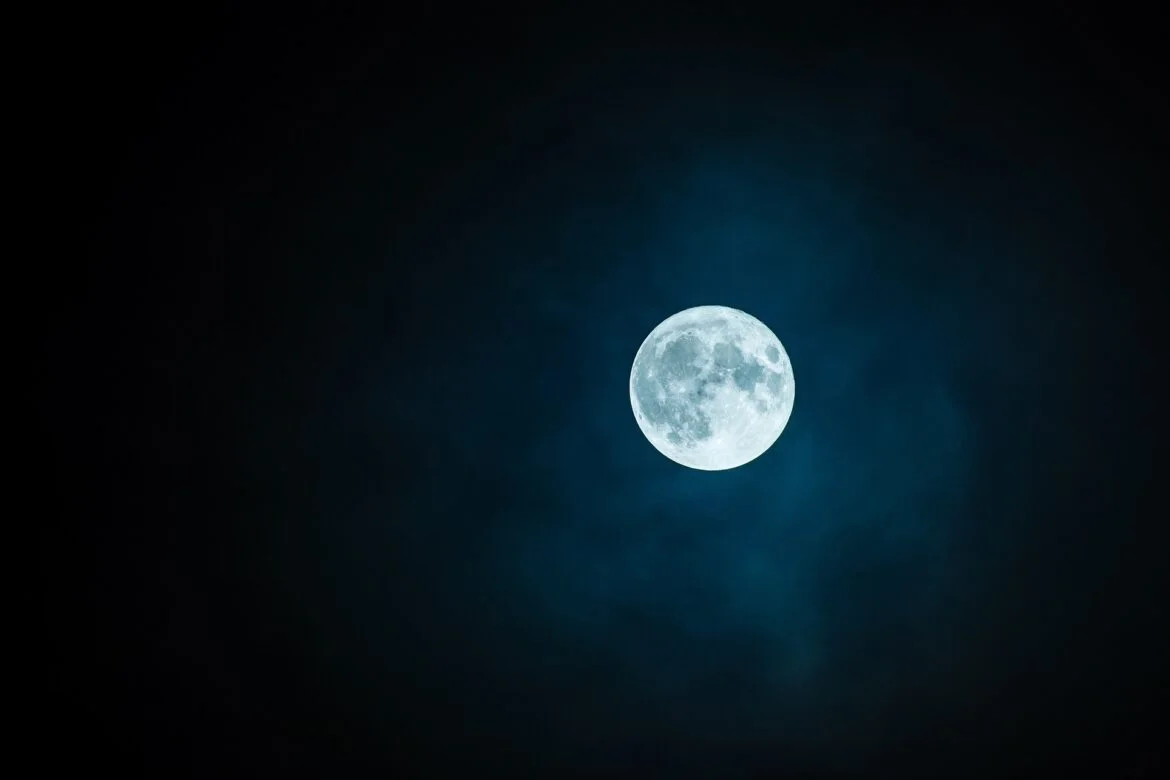 Full moon glowing blue in a dark night sky with wispy clouds.