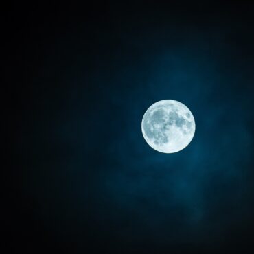 Full moon glowing blue in a dark night sky with wispy clouds.