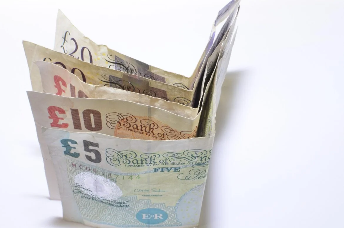 Stack of British pound notes fanned out on a white background, showing £5, £10, £20 and £50 notes to convey money.