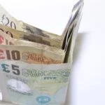 Stack of British pound notes fanned out on a white background, showing £5, £10, £20 and £50 notes to convey money.