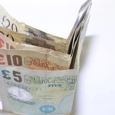 Stack of British pound notes fanned out on a white background, showing £5, £10, £20 and £50 notes to convey money.
