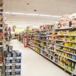 A supermarket aisle filled with shelves of canned goods, primarily Goya, on both sides under bright overhead lights.