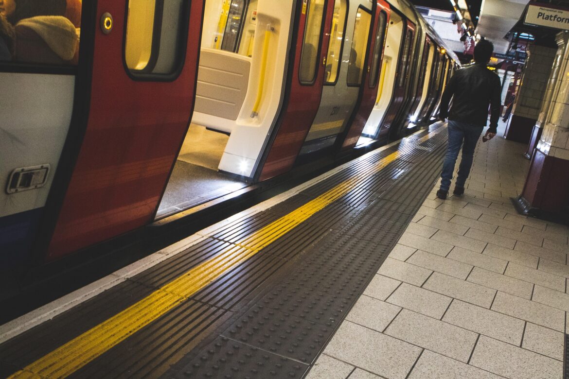 Subway platform with a red-and-gray train stopped at the platform; a man stands near the open doors.